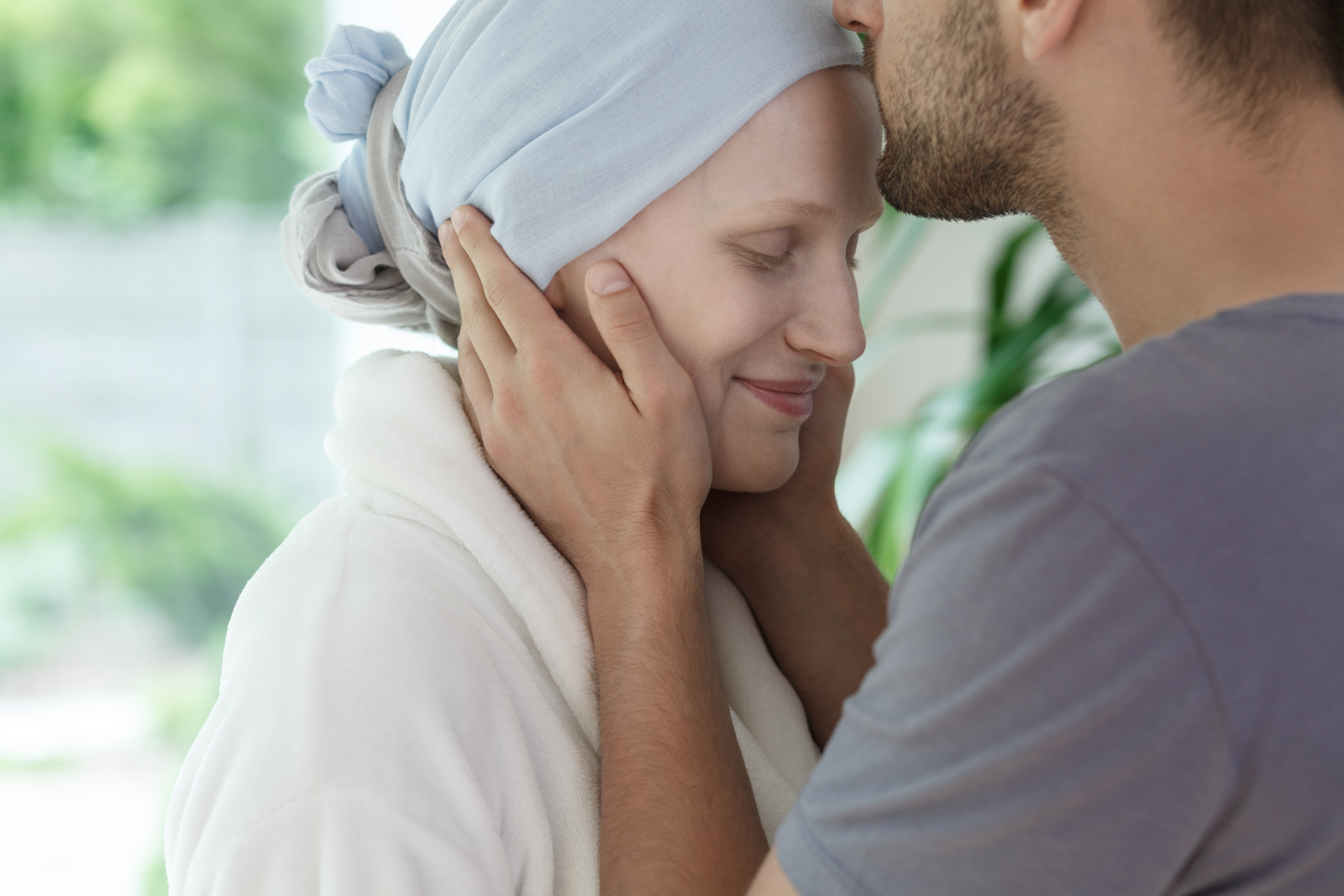 Une homme embrasse le front d’une femme atteinte d’un cancer
