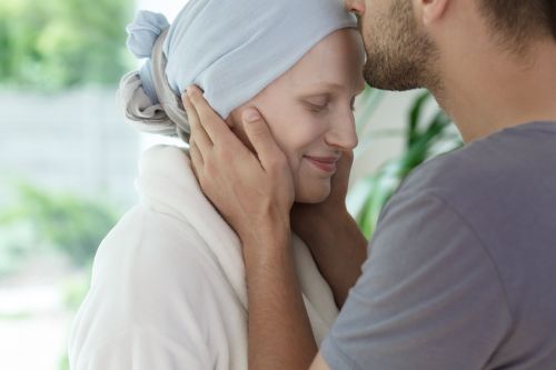 Photographie d’un couple où l’homme dépose un baiser sur le front de sa compagne atteinte d’un cancer.