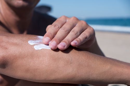 Photographie d'une personne à la plage, appliquant de la crème solaire sur sa peau. 