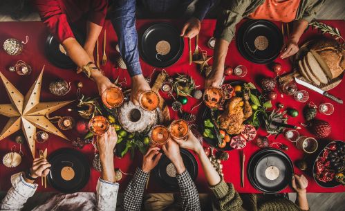 Photographie en plongée d’une table de dîner de fin d’année, où des convives trinquent avec des verres d’alcool, la table étant abondamment garnie de mets.