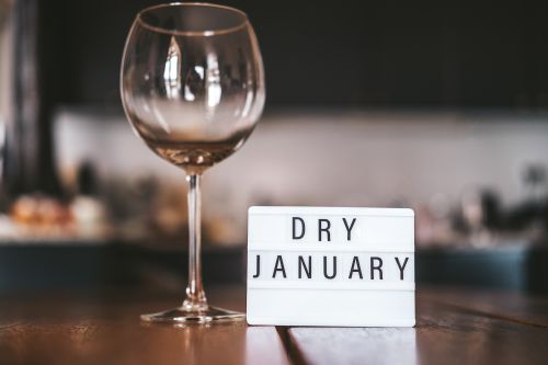 Photographie d’un verre vide posé sur une table, accompagné d’une pancarte décorative “Dry January